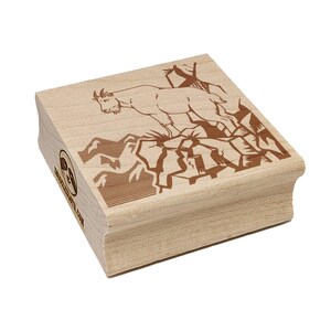 May include: A wooden stamp featuring a mountain goat standing on a rocky cliff. The goat and the rocky terrain are depicted in a brown color. The stamp has rounded edges and the text "www.etsy.com" is visible on the side.