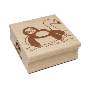 May include: A wooden stamp featuring a brown illustration of a sloth floating on a swan-shaped inflatable ring. The stamp has a light wood grain finish and the text "www.etsy.com" is visible on the side.