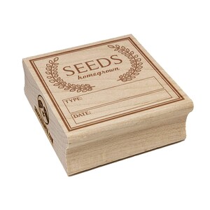 May include: A rectangular wooden stamp with the word "SEEDS" in a decorative font, framed by a laurel wreath. Below, it has spaces for "TYPE:" and "DATE:" in a brown ink. The stamp is for homegrown seeds.