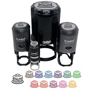May include: A collection of black Trodat self-inking stamps with a pancake design. The stamps vary in size and include the text "Trodat" and "printy 46042". Below the stamps are several pancake illustrations in various colors.