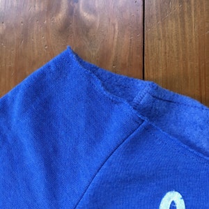 May include: Close-up of the shoulder seam of a royal blue sweatshirt. The seam is sewn with a zig-zag stitch.