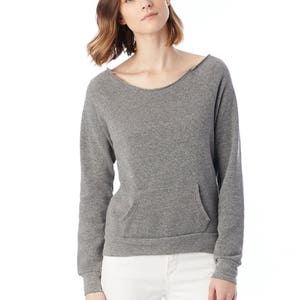 May include: A heather gray sweatshirt with a wide, slightly distressed neckline and long sleeves. The sweatshirt features a kangaroo pocket on the front. The model is wearing white distressed jeans.