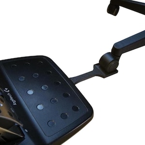 Peut inclure: Pédales de course Logitech noires avec un repose-pieds texturé et plusieurs boutons. Les pédales sont fixées à un bras en métal noir avec une roue.