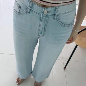 Puede incluir: Vaqueros de mezclilla azul claro con dise&ntilde;o de cintura alta, cierre de bot&oacute;n, cremallera y estilo cl&aacute;sico de cinco bolsillos. Los pantalones tienen un corte recto y un acabado de lavado claro, combinados con un top de punto a rayas.