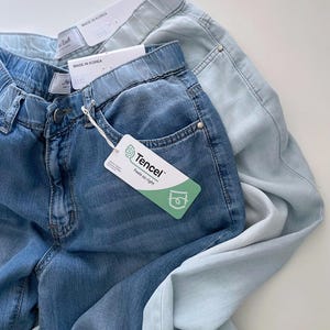 Puede incluir: Dos pantalones vaqueros con cintura el&aacute;stica, uno en tono azul medio y otro en azul claro. Ambos tienen etiquetas blancas que dicen Made in Korea y una etiqueta Tencel en el pantal&oacute;n azul medio con el texto Tencel Feels so right.