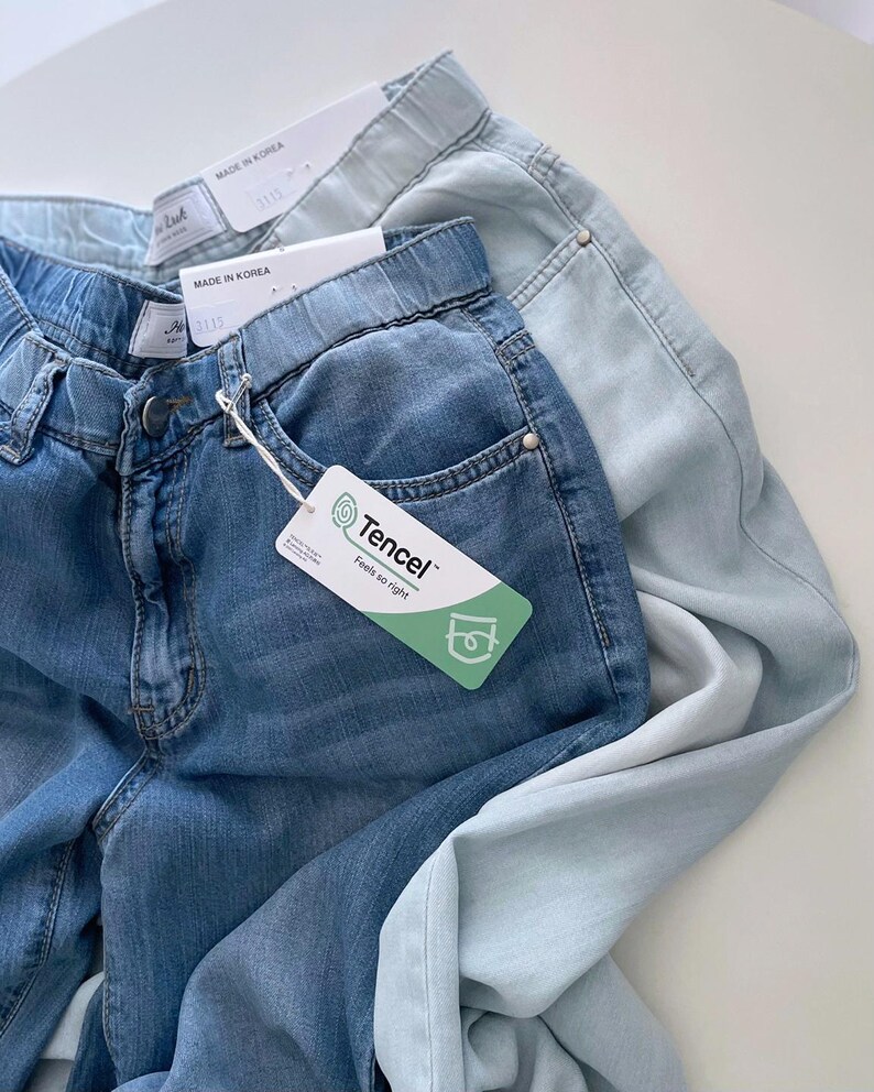 Puede incluir: Dos pantalones vaqueros con cintura el&aacute;stica, uno en tono azul medio y otro en azul claro. Ambos tienen etiquetas blancas que dicen Made in Korea y una etiqueta Tencel en el pantal&oacute;n azul medio con el texto Tencel Feels so right.