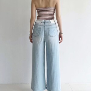 Puede incluir: Unos vaqueros de pernera ancha en color azul claro con cintura alta y dos bolsillos traseros. La cintura lleva una etiqueta blanca con el texto HOWLUK. Los vaqueros se combinan con un top halter de rayas horizontales en tonos rosa, marr&oacute;n y blanco.