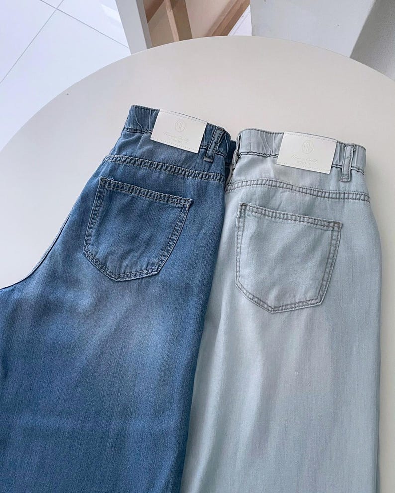 Puede incluir: Dos pares de pantalones vaqueros en tonos azul medio y azul claro. Cada par cuenta con una cintura el&aacute;stica, trabillas para cintur&oacute;n, un bolsillo trasero y una etiqueta de marca rectangular blanca cosida en la parte posterior.