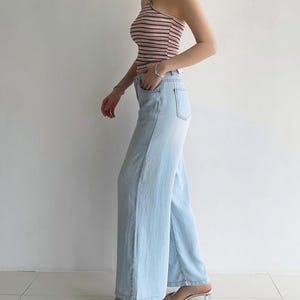 Puede incluir: Un top halter sin mangas con rayas horizontales en tonos rosa, blanco y negro, combinado con pantalones vaqueros de mezclilla azul claro de corte ancho. Los pantalones tienen un dise&ntilde;o cl&aacute;sico de cinco bolsillos con cierre de bot&oacute;n y cremallera.