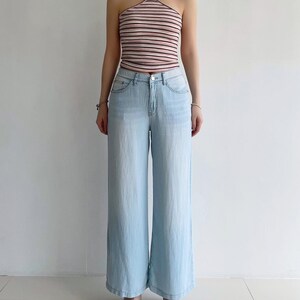 Puede incluir: Un top de cuello halter con rayas horizontales en tonos rosa, blanco y negro, combinado con unos vaqueros de mezclilla azul claro. Los vaqueros tienen una silueta de pierna ancha, cierre cl&aacute;sico de bot&oacute;n y cremallera, y cinco bolsillos.