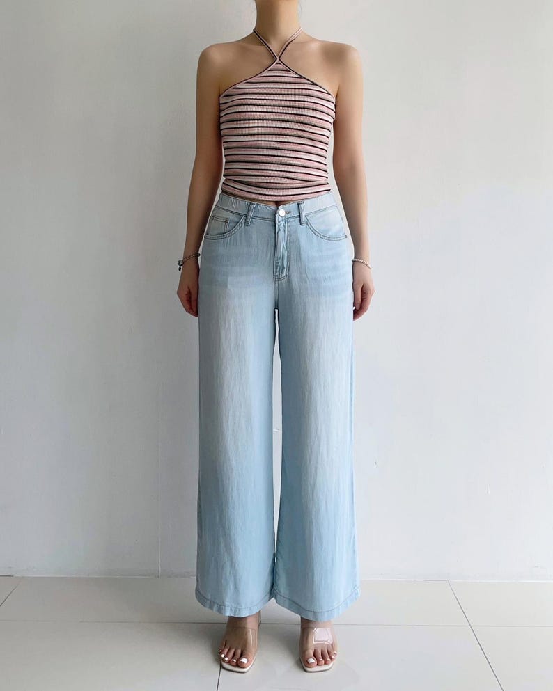 Puede incluir: Un top de cuello halter con rayas horizontales en tonos rosa, blanco y negro, combinado con unos vaqueros de mezclilla azul claro. Los vaqueros tienen una silueta de pierna ancha, cierre cl&aacute;sico de bot&oacute;n y cremallera, y cinco bolsillos.