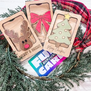 May include: Three wooden Christmas card holders with a reindeer, a bow, and a Christmas tree. The cards are decorated with the text "Merry & Bright" and "Merry Christmas". A gift card with the text "Fun Main Event" is also visible.