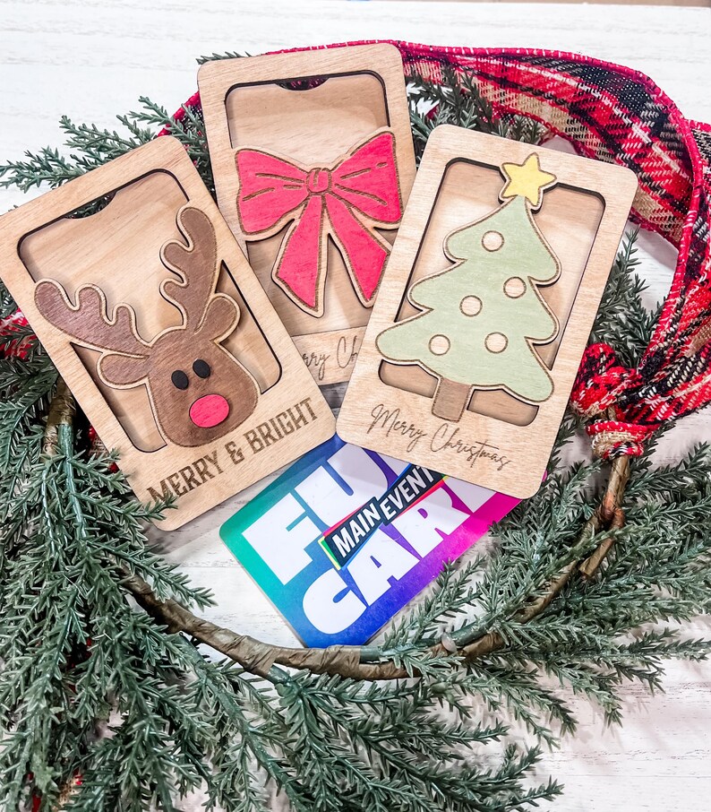 May include: Three wooden Christmas card holders with a reindeer, a bow, and a Christmas tree. The cards are decorated with the text "Merry & Bright" and "Merry Christmas". A gift card with the text "Fun Main Event" is also visible.