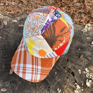 May include: A patchwork baseball cap with a brown, orange, red, yellow, blue, and white floral pattern. The brim of the cap is a brown and white plaid.