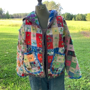 May include: A patchwork jacket with a hood, featuring a variety of colorful fabrics and green yarn embellishments. The jacket has a button closure and two pockets.