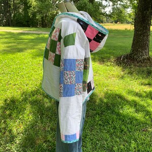 May include: A white quilted jacket with a hood. The jacket is made of patchwork fabric in various colors and patterns, including green, pink, blue, and floral. The jacket has a white lining and a blue trim.