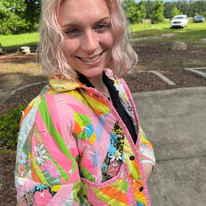May include: A colorful patchwork jacket with a vibrant mix of pink, green, orange, and floral patterns. The jacket features a quilted design, black buttons, and a pink trim along the edges. The jacket is a unique piece of clothing.