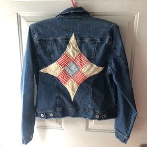 May include: A blue denim jacket with a large patchwork star on the back. The star is made of red, white, and blue fabric.