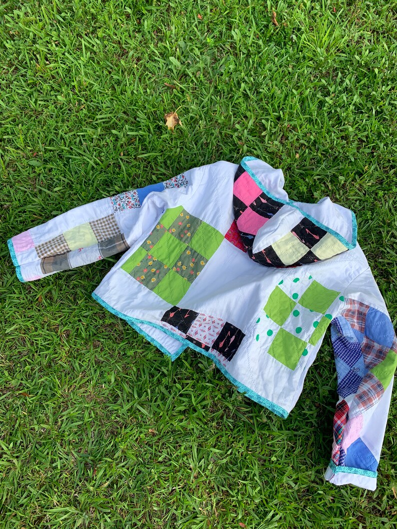 May include: A white quilted jacket with a patchwork design. The jacket has a hood and long sleeves. The patchwork is made of different colored fabrics, including green, pink, blue, and red.