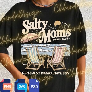 May include: Black t-shirt with a beach-themed graphic. The design features the words "Salty Moms Beach Club" above an illustration of beach chairs, an umbrella, and ocean waves. The phrase "GIRLS JUST WANNA HAVE SUN" is printed below.