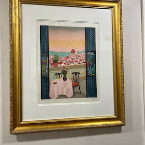 May include: A framed print of a painting depicting a table with a red and white checkered tablecloth set for two on a balcony overlooking a cityscape. The cityscape includes a large dome building in the distance. The balcony is decorated with potted plants and flowers.