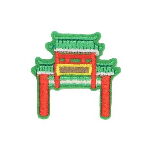 Puede incluir: Un parche bordado que representa una puerta torii japonesa tradicional. La puerta está hecha de madera y tiene un techo rojo con detalles amarillos. La puerta está rodeada de vegetación verde.