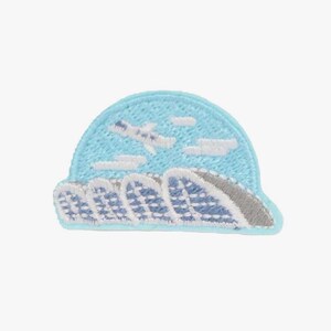 May include: A semi-circular embroidered patch featuring a light blue sky with white clouds and a small white airplane flying above a series of stylized blue and white ocean waves with a grey accent on the right side of the wave pattern.