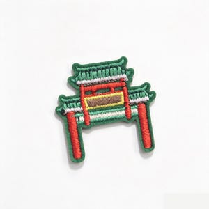 Puede incluir: Un parche bordado con el diseño de una puerta tradicional de Asia Oriental. El parche muestra pilares verticales de color rojo vibrante, una estructura de techo de tejas verdes y un panel central rectangular en tonos amarillo y marrón.