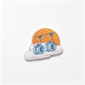 May include: An embroidered patch featuring two light blue cable cars suspended by dark blue lines against a bright orange circular sun, all resting atop a white cloud shape with a white border, creating a detailed and colorful graphic design.