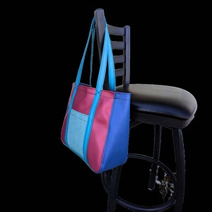 May include: A blue, pink, and teal tote bag with a pocket hanging on a black chair.