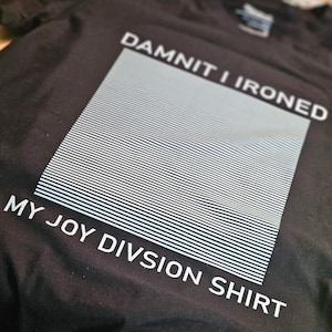 Könnte beinhalten: Schwarzes T-Shirt mit weißem Text, der "Damn it I ironed my Joy Division shirt" lautet. Der Text befindet sich in einem Quadrat mit einem weißen Streifenmuster.