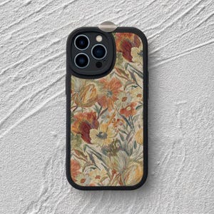 May include: A black smartphone case featuring a rectangular back panel with a detailed floral pattern in shades of orange, yellow, cream, and muted green. The case has a black camera cutout section with three circular lenses and a flash component.