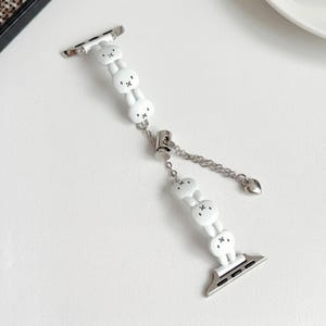 May include: White watch strap with a bunny design. The strap features a series of white bunny figures with black facial details, connected by a silver chain and clasp. A small heart charm dangles from the chain.