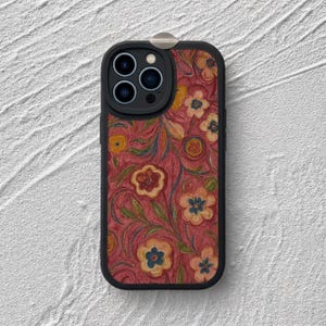 May include: A black smartphone case featuring a textured, reddish-pink background with a repeating pattern of stylised flowers in shades of yellow, orange, and blue, accented by green leaves and swirling vine-like stems across the entire surface.
