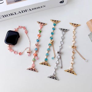 May include: A collection of decorative watch bands in various colors. The bands feature beaded and chain designs with gold, silver, and rose gold connectors. One band is attached to a black smartwatch.