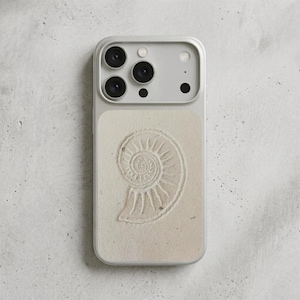 Op de afbeelding: Een lichtgrijze smartphonehoes met een beige achterpaneel voorzien van een gedetailleerd, gegraveerd spiraalvormig schelpontwerp. De hoes heeft een verhoogde uitsparing voor de cameramodule met drie ronde lensopeningen, een flitser en een sensor.