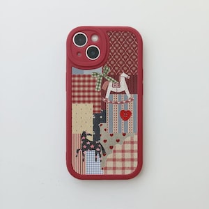 Può includere: Custodia per telefono rossa con un design patchwork con un cavallo a dondolo, cuori e sagome di cavalli. La custodia ha un anello per fotocamera rosso e una varietà di motivi in tessuto nei colori rosso, blu e crema.