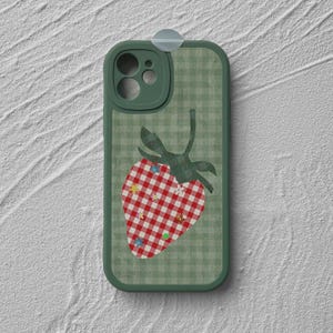 May include: A green phone case with a gingham pattern and a red and white checkered strawberry design. The strawberry has a green stem and is decorated with small colorful stars and flowers.