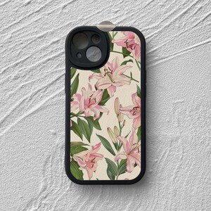 May include: A black phone case with a floral design featuring pink lilies on a cream background. The case has a cutout for the camera lens.