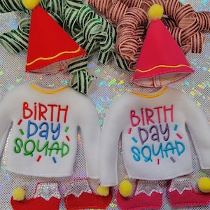 May include: Two elf outfits with white long-sleeved shirts that say "BIRTHDAY SQUAD" in colorful letters. Each outfit includes a red and white hat, red shoes with yellow pom-poms, and silver glitter accents.