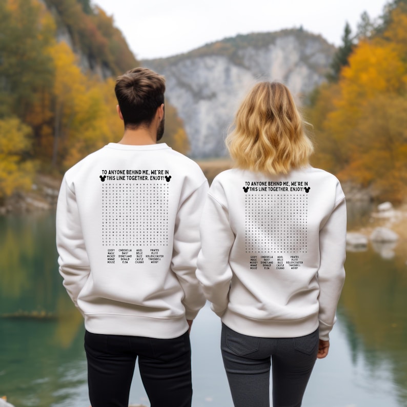 May include: Two white sweatshirts with a word search design on the back. The text on the sweatshirts reads "TO ANYONE BEHIND ME, WE'RE IN THIS LINE TOGETHER. ENJOY!" with a Mickey Mouse head. The sweatshirts are worn by two people.