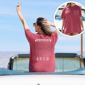 May include: A maroon t-shirt featuring a white Mickey Mouse head on the front and text on the back. The back of the shirt has the text "TO ANYONE BEHIND ME, WE'RE IN THIS LINE TOGETHER. ENJOY!" with a grid of dots and more text.