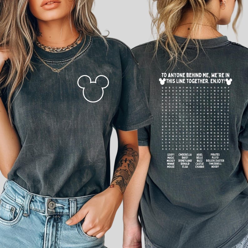May include: Dark grey t-shirt with a white Mickey Mouse outline on the front. The back displays the text "TO ANYONE BEHIND ME, WE'RE IN THIS LINE TOGETHER. ENJOY!" and a Disney-themed word search.