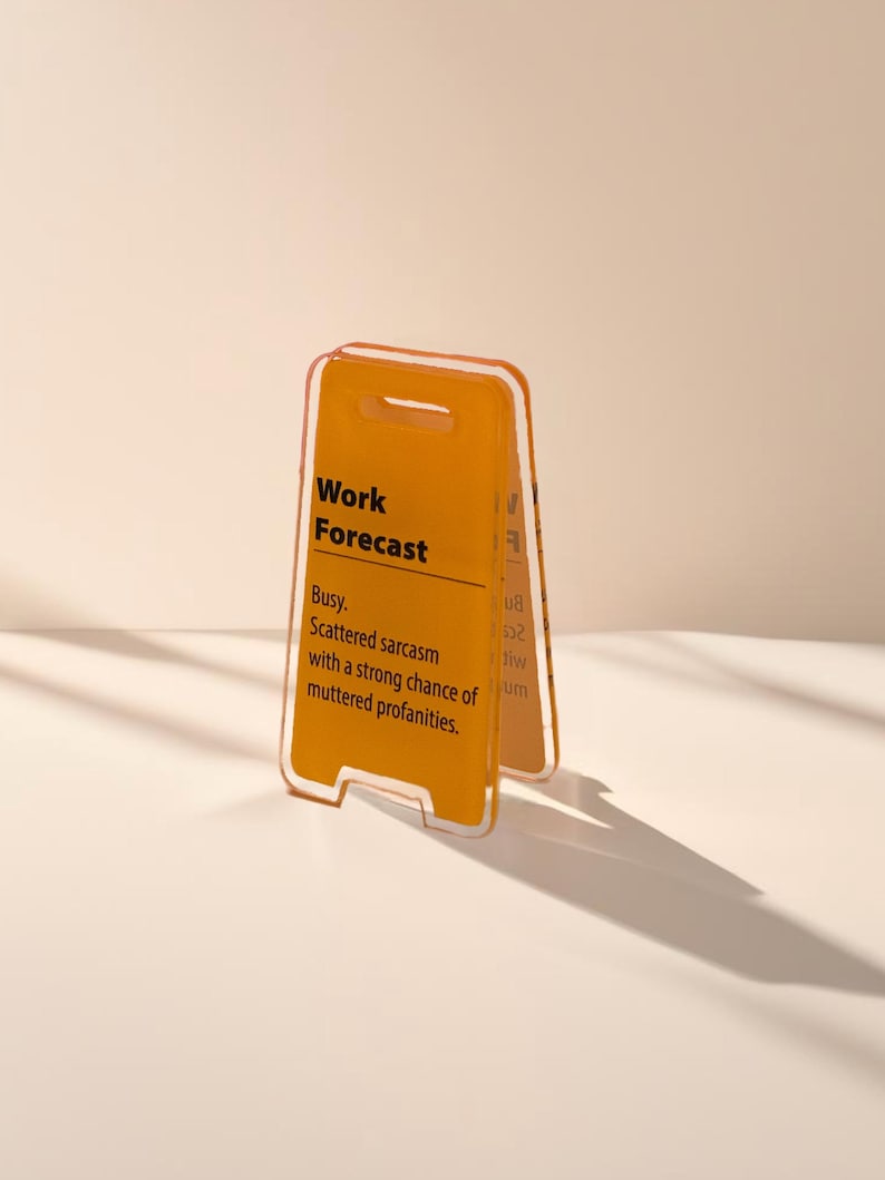 May include: A yellow and orange plastic sign with the text "Work Forecast" and the description "Busy. Scattered sarcasm with a strong chance of muttered profanities."