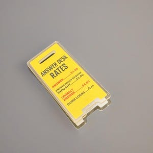 Può includere: Un cartello giallo con testo nero che recita "Answer Desk Rates". Il cartello elenca diverse tariffe per rispondere alle domande, con prezzi che vanno da 1,00 € a 4,00 €. Il cartello indica anche che "Dumb Looks... free".