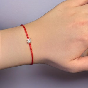 Op de afbeelding: Een rood koord armbandje met een kleine, heldere edelsteen bedel.