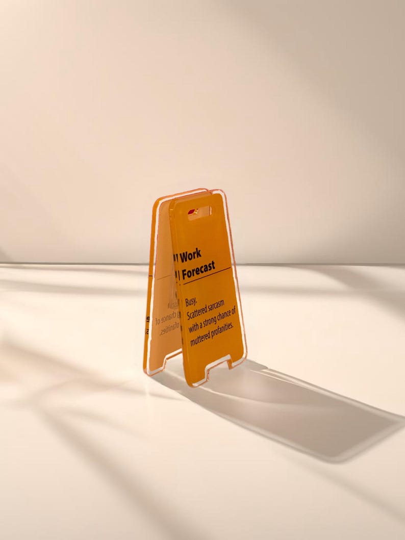 May include: A yellow plastic sign with the text "Work Forecast" and the description "Busy. Scattered sarcasm with a strong chance of muttered profanities."