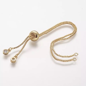 May include: Gold chain bracelet with a round bead and two small clear stones. The chain is adjustable with a sliding bead.