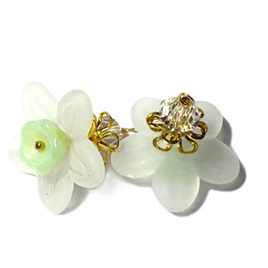 May include: A pair of white flower-shaped earrings with a green center and gold accents.