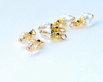 Op de afbeelding: Een set van vijf heldere kristallen en goudkleurige kralenbedels. De bedels zijn traanvormig en hebben een goudkleurige lus aan de bovenkant.